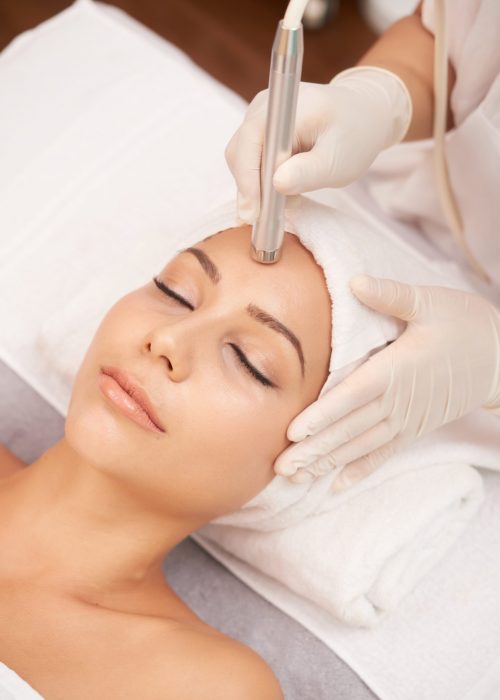 Relaxed woman lying in beauty salon and having anti-wrinkle therapy on her forehead