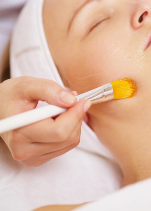 Close-up shot of a woman being applied a facial mask by cosmetician at beauty spa